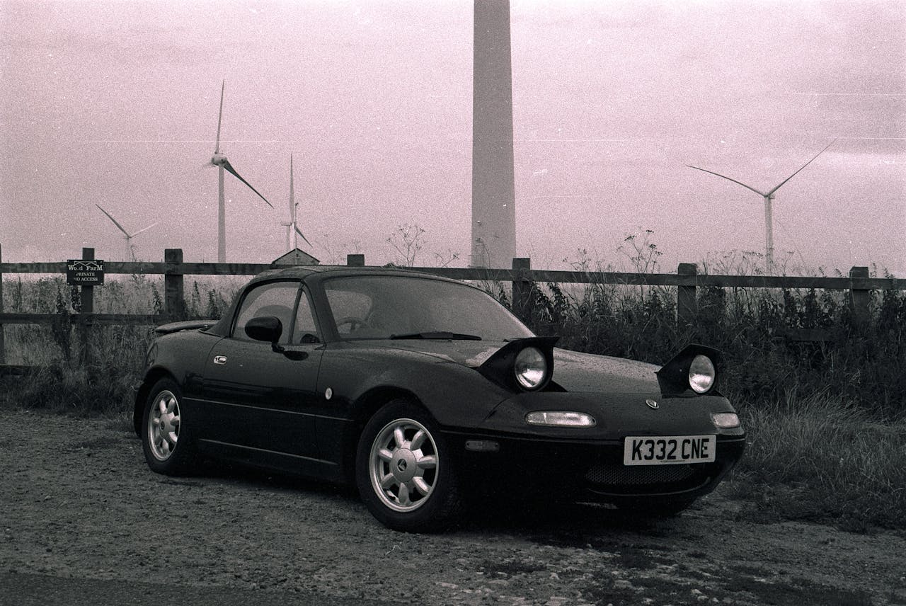 A classic Mazda MX-5 parked outdoors surrounded by wind turbines, capturing a retro automotive scene.